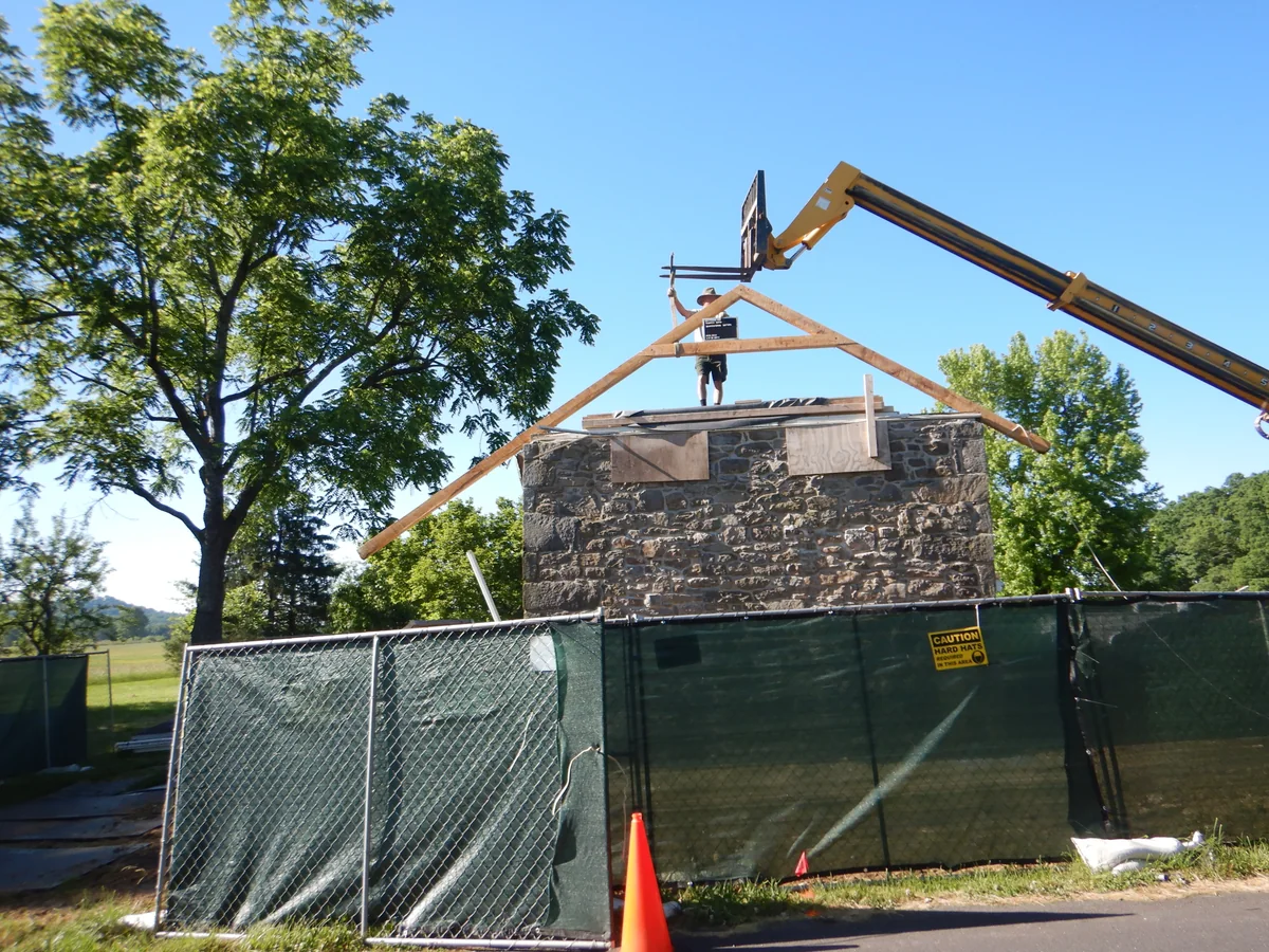 Exposed timber roof frame above historic stone walls, with a telehandler and construction fence.